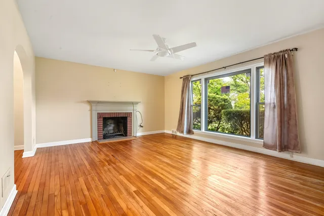 a view of an empty room with wooden floor fireplace and a window