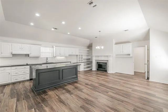 a large kitchen with granite countertop a stove top oven a sink and white cabinets with wooden floor