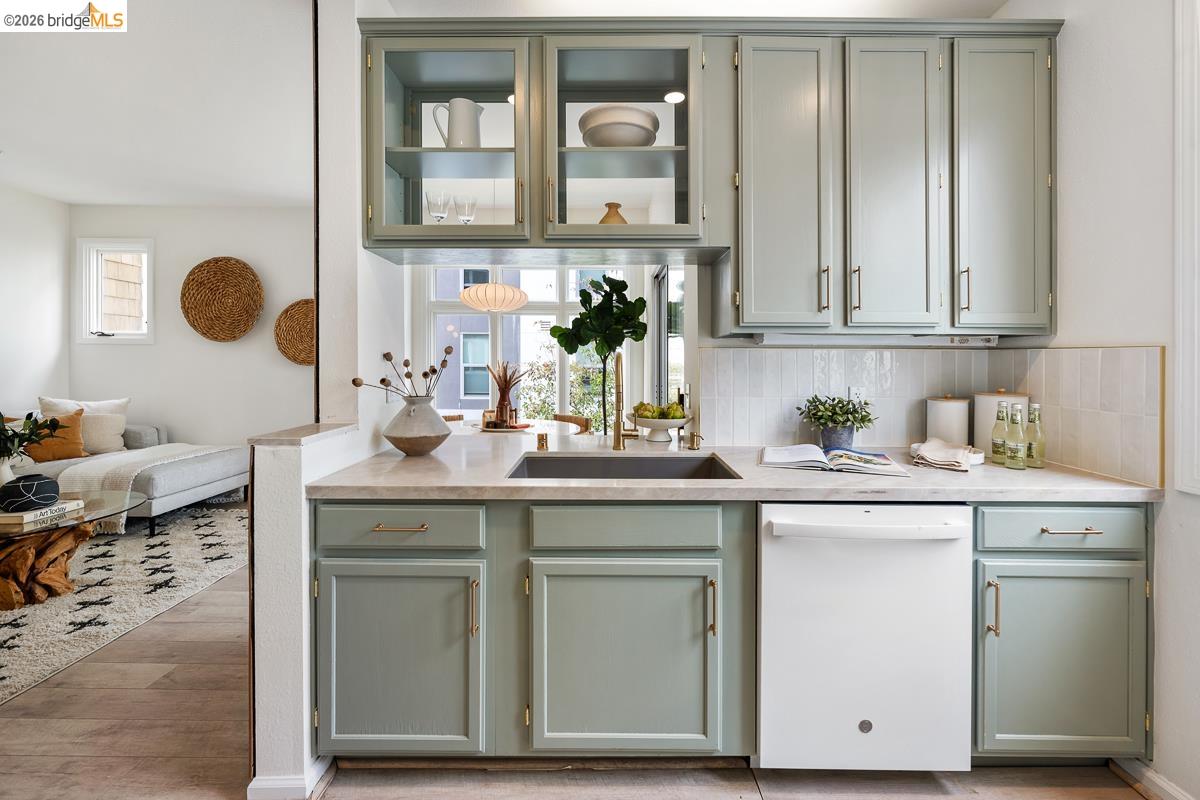 2029 Channing Way, Unit 3D Berkeley, CA 94704 - Photo 19 of 54 Kitchenette featuring light green cabinetry, clear glass upper cabinets, a built-in sink with a gold-tone faucet, and a white dishwasher