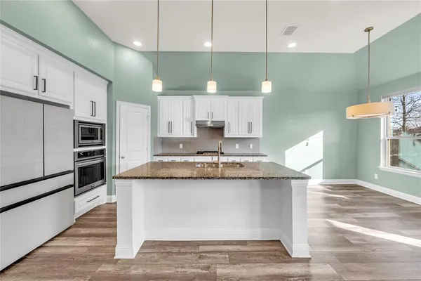 a view of a kitchen with kitchen island a sink wooden floor and stainless steel appliances