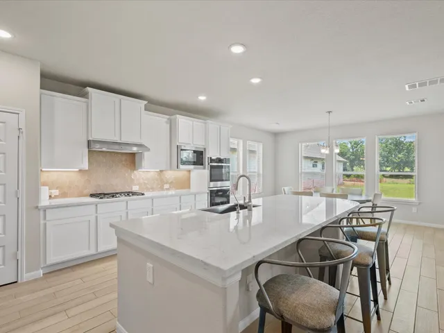 a kitchen with stainless steel appliances granite countertop a stove a sink a refrigerator white cabinets and couches with wooden floor