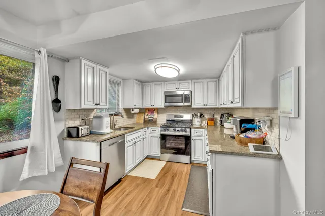 a kitchen with stainless steel appliances granite countertop a stove top oven a sink dishwasher and white cabinets with wooden floor