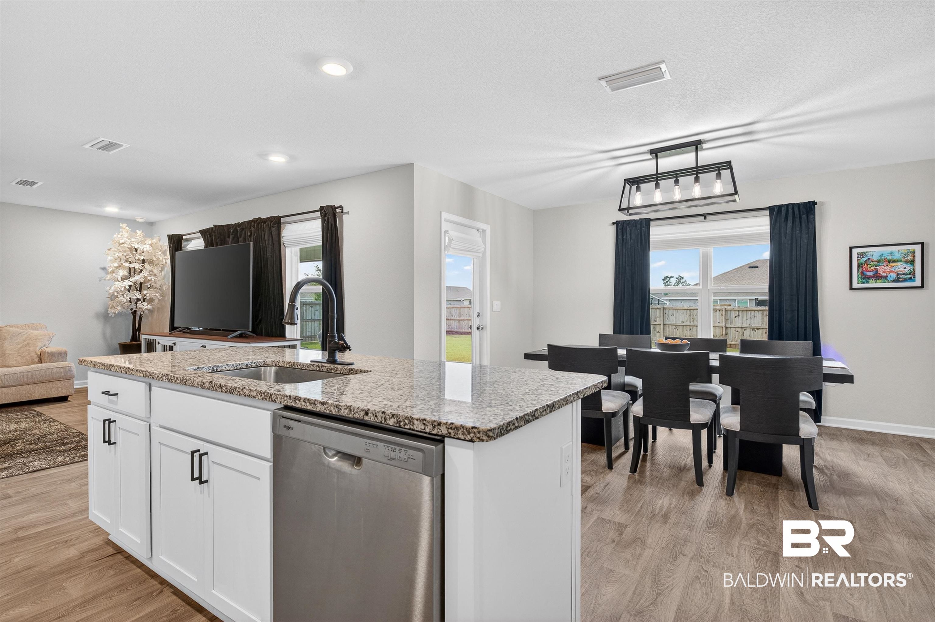 3213 Camino Real Loop Lillian, AL 36549 - Photo 34 of 61 Kitchen island featuring a stainless steel sink with a black gooseneck faucet, light granite countertop, white cabinetry with black hardware, and an integrated stainless steel dishwasher
