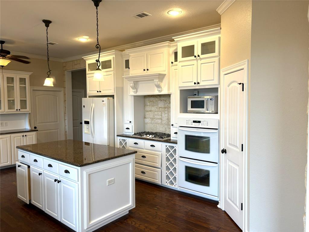 1170 Brazos Loop Gholson, TX 76705 - Photo 18 of 37 Kitchen featuring white cabinetry and dark hardware, a center island with a stone-finish countertop, stainless steel refrigerator, built-in double ovens, and a gas cooktop with a brick-patterned backsplash