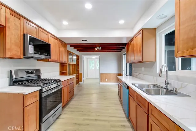 a kitchen with stainless steel appliances granite countertop a stove top oven a sink dishwasher a microwave oven and a refrigerator with wooden cabinets