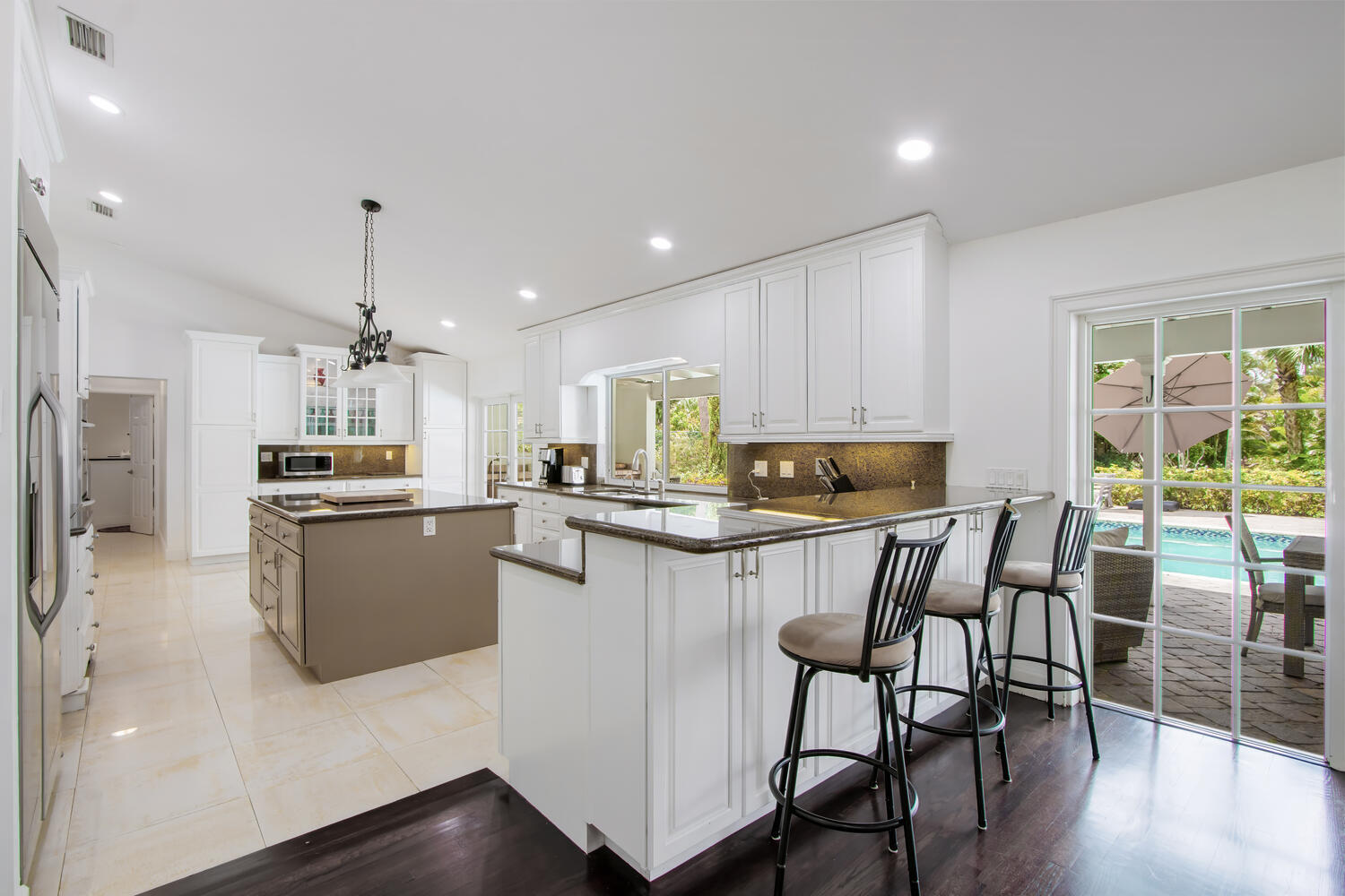 12327 Quercus Lane Wellington, FL 33414 - Photo 8 of 34 a kitchen with kitchen island granite countertop wooden floors white cabinets and stainless steel appliances