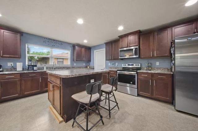 a kitchen with kitchen island granite countertop wooden cabinets a counter top space a sink and appliances