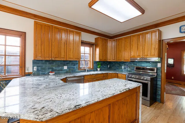 a kitchen with stainless steel appliances granite countertop wooden cabinets a stove a sink and a large window