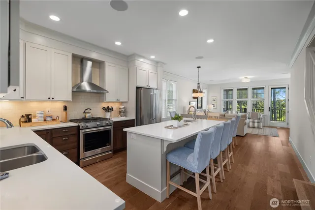 a open kitchen with stainless steel appliances granite countertop a stove top oven a sink dishwasher a dining table and chairs with wooden floor