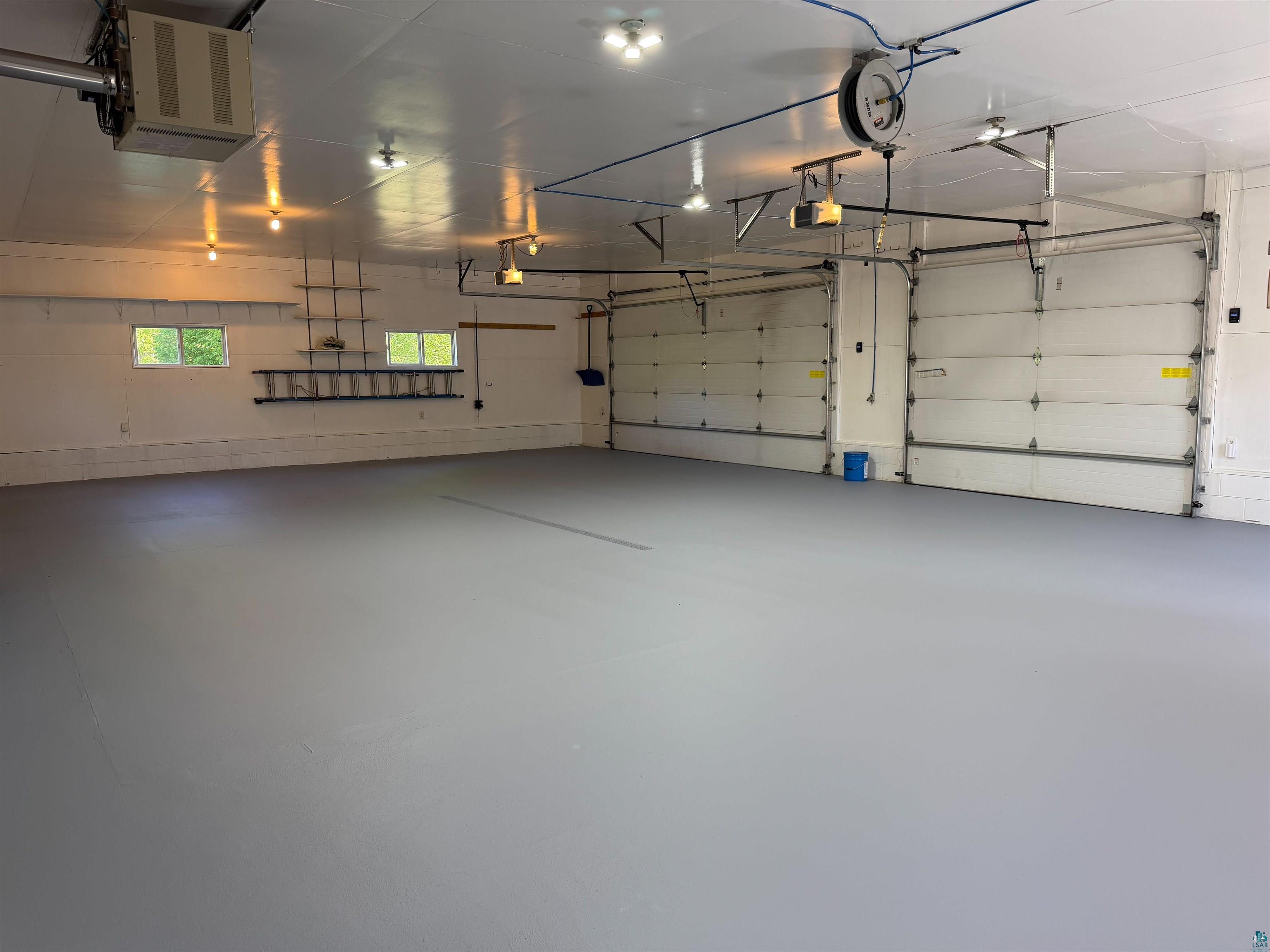 11702 East Mail Road Gordon, WI 54838 - Photo 60 of 60 Spacious garage featuring a light grey floor finish, white walls, multiple overhead lighting fixtures, two garage doors, and natural light from two windows