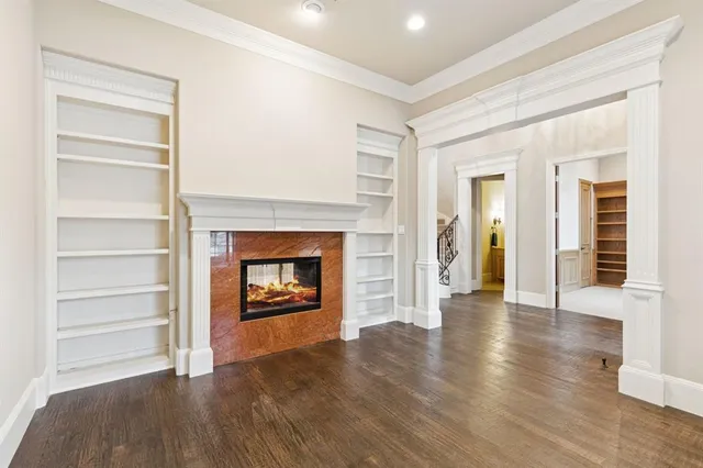 a view of an empty room with wooden floor fire place and windows