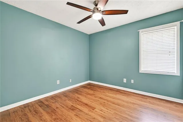 an empty room with wooden floor fan and windows