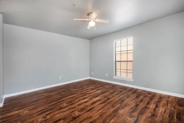 a view of an empty room with wooden floor and a window