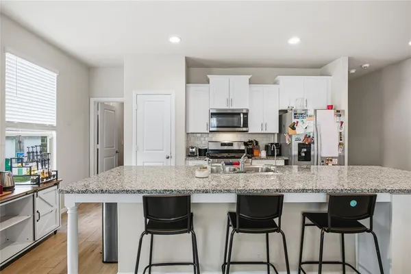 a kitchen with stainless steel appliances granite countertop a stove top oven a sink dishwasher and a refrigerator with wooden floor