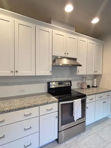 a kitchen with granite countertop white cabinets and a stove