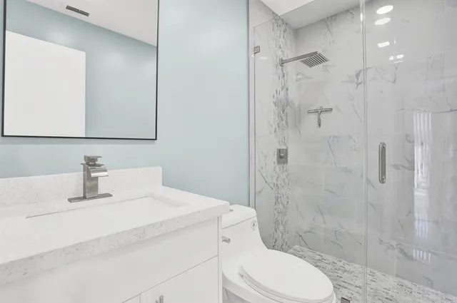 a bathroom with a toilet sink vanity granite and shower