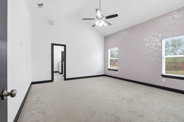 an empty room with chandelier fan and windows