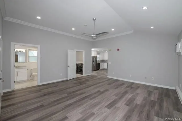 a view of an empty room with wooden floor and a kitchen
