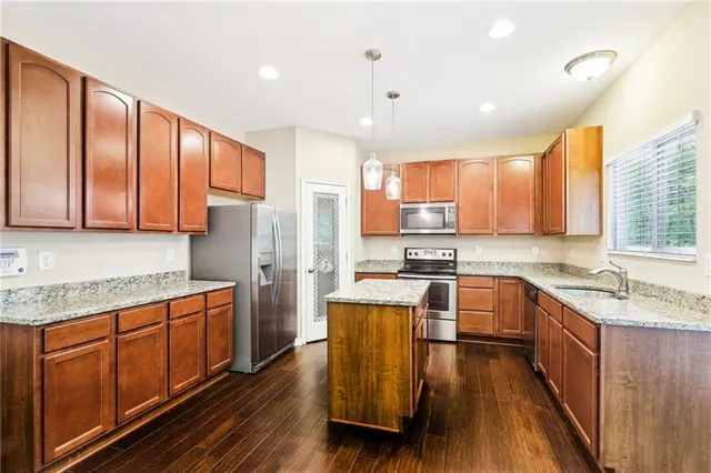 a kitchen with stainless steel appliances granite countertop wooden cabinets a refrigerator a sink a stove and wooden floors