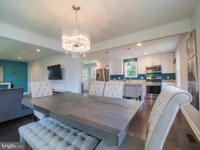 a living room with stainless steel appliances furniture a chandelier and a kitchen view