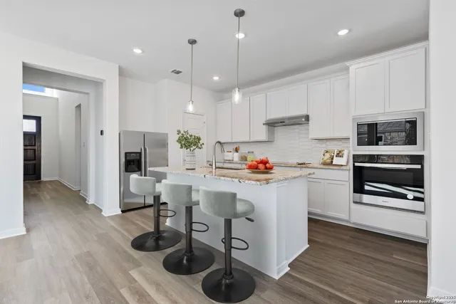 a kitchen with stainless steel appliances granite countertop a refrigerator oven a sink dishwasher and white cabinets with wooden floor