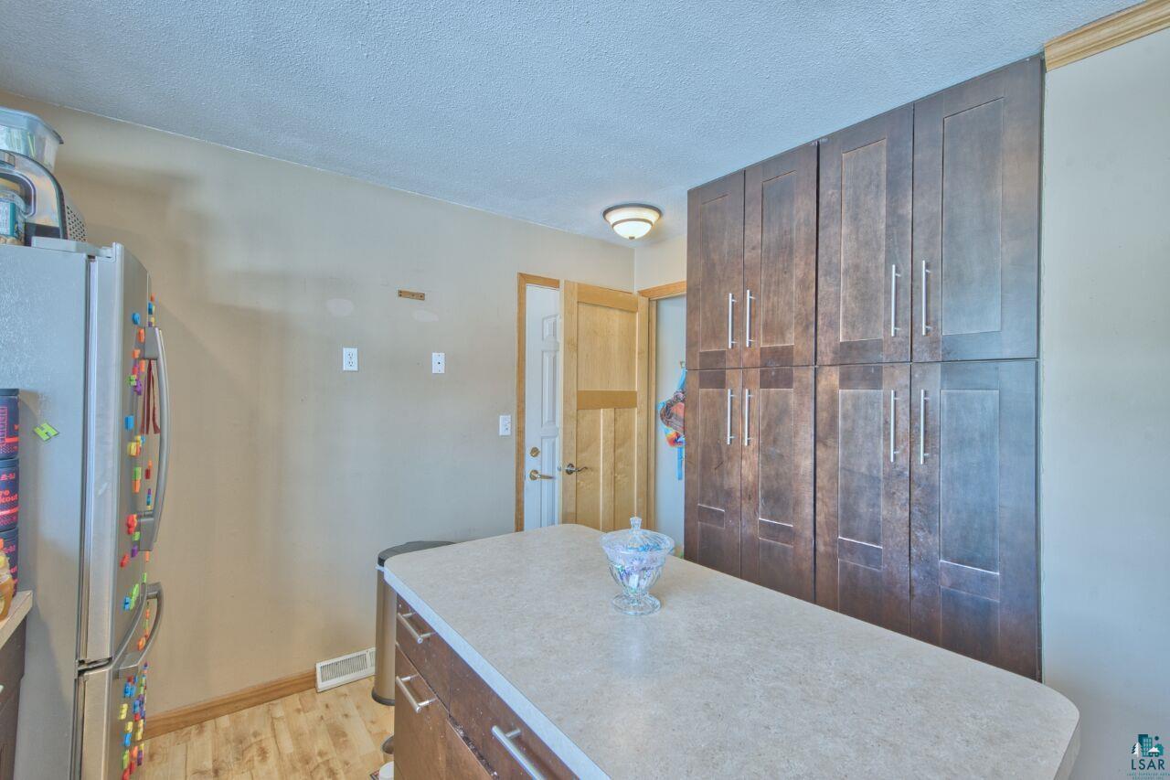 203 Wyandotte Road Hoyt Lakes, MN 55750 - Photo 14 of 44 Kitchen featuring freestanding refrigerator, a textured ceiling, light countertops, light wood-style flooring, and a kitchen island
