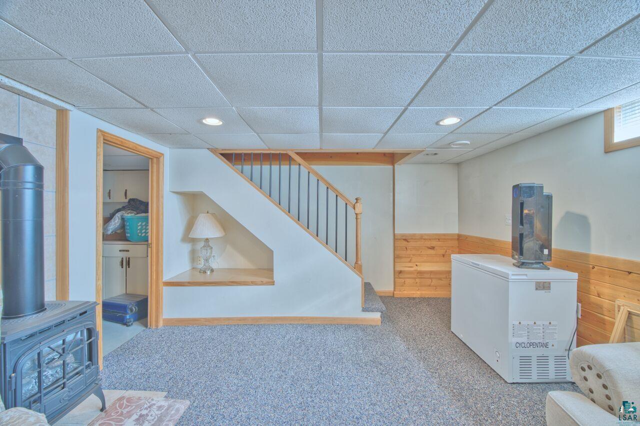 203 Wyandotte Road Hoyt Lakes, MN 55750 - Photo 20 of 39 Finished basement featuring carpet, wood walls, white fridge, a paneled ceiling, and a wood stove