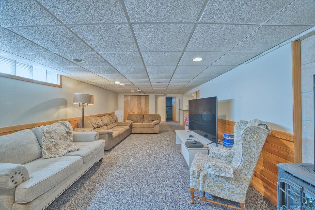203 Wyandotte Road Hoyt Lakes, MN 55750 - Photo 21 of 39 Carpeted living area featuring a paneled ceiling, a wainscoted wall, a wood stove, wood walls, and recessed lighting