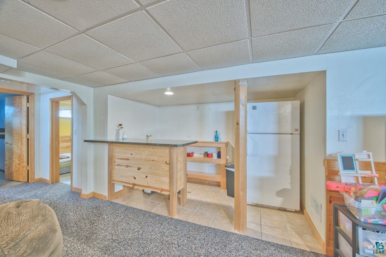 203 Wyandotte Road Hoyt Lakes, MN 55750 - Photo 23 of 44 Indoor dry bar featuring freestanding refrigerator, a paneled ceiling, dark countertops, light tile patterned floors, and light wood finish cabinets
