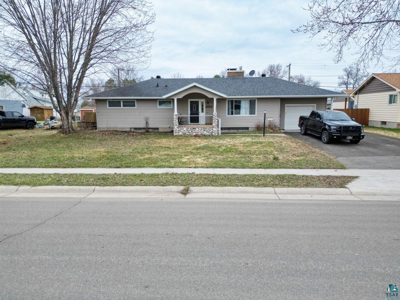 203 Wyandotte Road Hoyt Lakes, MN 55750 - Photo 28 of 39 Ranch-style residence featuring light-toned siding, a covered porch with stone columns, an attached garage, a paved driveway, and a shingled roof