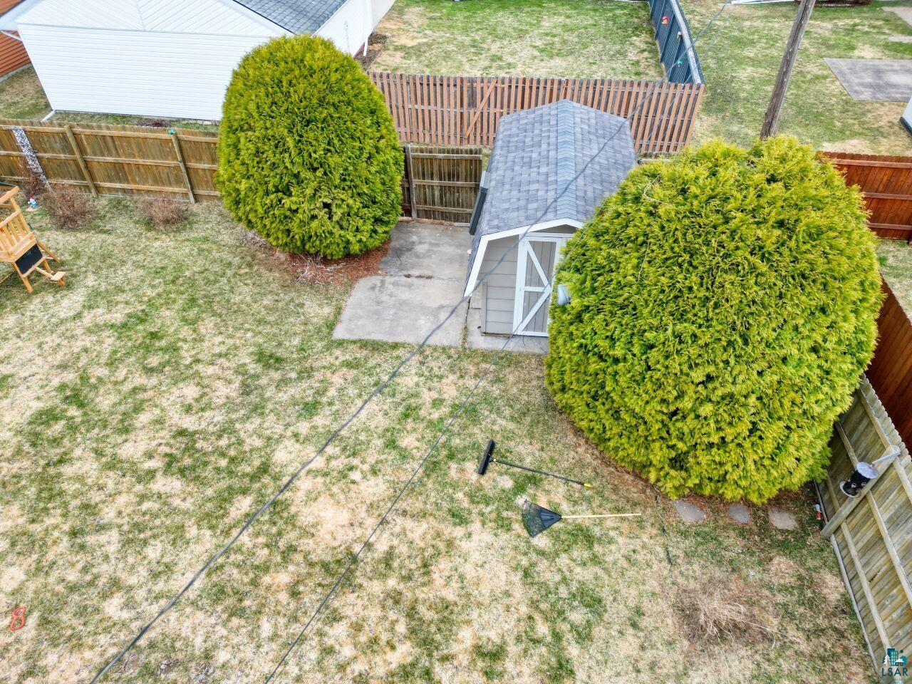 203 Wyandotte Road Hoyt Lakes, MN 55750 - Photo 32 of 39 Expansive backyard featuring a fenced perimeter, two mature evergreen shrubs, a paved patio area, and a storage shed with an asphalt shingle roof