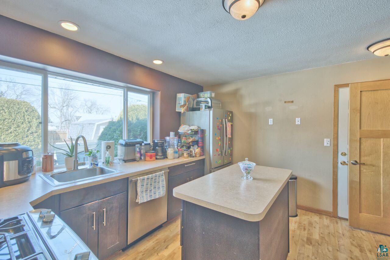 203 Wyandotte Road Hoyt Lakes, MN 55750 - Photo 10 of 44 Kitchen with stainless steel appliances, light countertops, light wood finished floors, a kitchen island, and dark wood finish cabinets