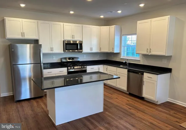 a kitchen with stainless steel appliances granite countertop a sink a stove a refrigerator and white cabinets