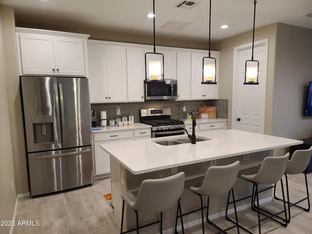 a kitchen with stainless steel appliances granite countertop a sink a stove a refrigerator and white cabinets with wooden floor