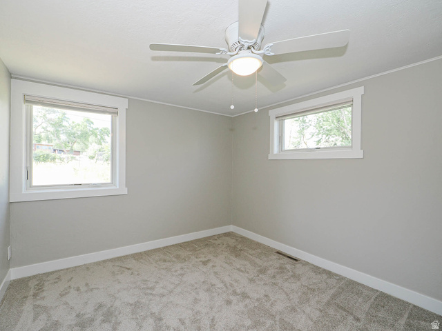 154 East 3000th Street South Bountiful, UT 84010 - Photo 17 of 37 Neutral-toned room featuring a ceiling fan with integrated lighting, two windows with white trim, light gray walls, and textured gray carpeting