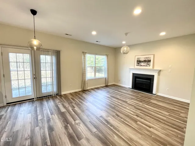 a view of an empty room with wooden floor fireplace and a window