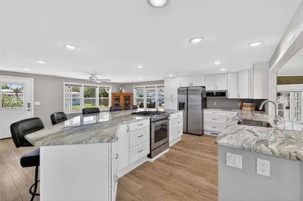 a large kitchen with stainless steel appliances granite countertop a stove a sink a refrigerator and white cabinets with wooden floor