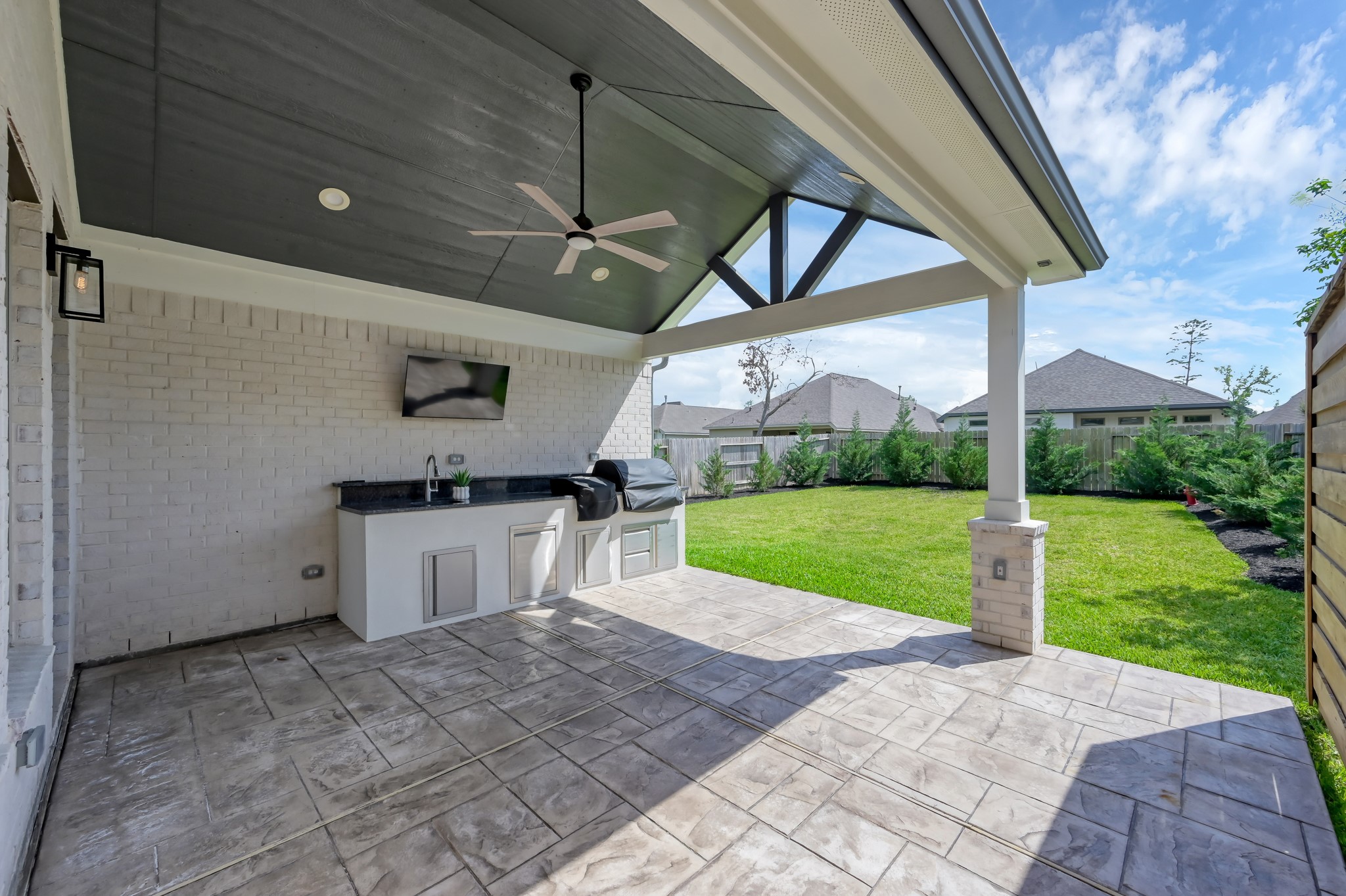 550 Chestnut Reef Court Conroe, TX 77304 - Photo 36 of 46 Spacious covered patio with outdoor kitchen, ceiling fan, and TV setup—perfect for entertaining while enjoying the private backyard.