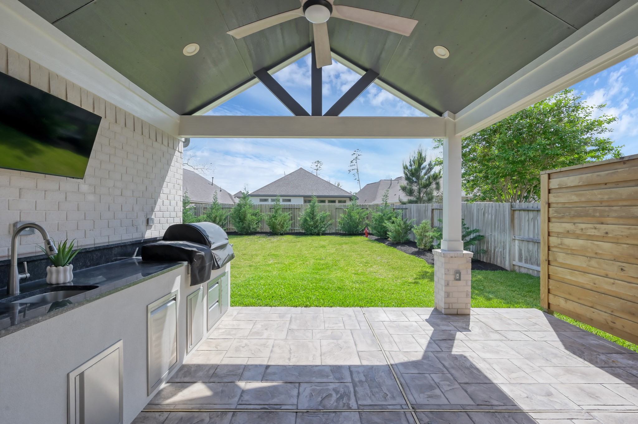 550 Chestnut Reef Court Conroe, TX 77304 - Photo 6 of 46 Spacious covered patio with outdoor kitchen, ceiling fan, and TV setup—perfect for entertaining while enjoying the private backyard.