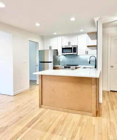 a view of a kitchen with kitchen island a sink wooden floor and stainless steel appliances