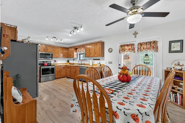 a view of a dining room and livingroom with furniture wooden floor a chandelier fan a kitchen view and a window