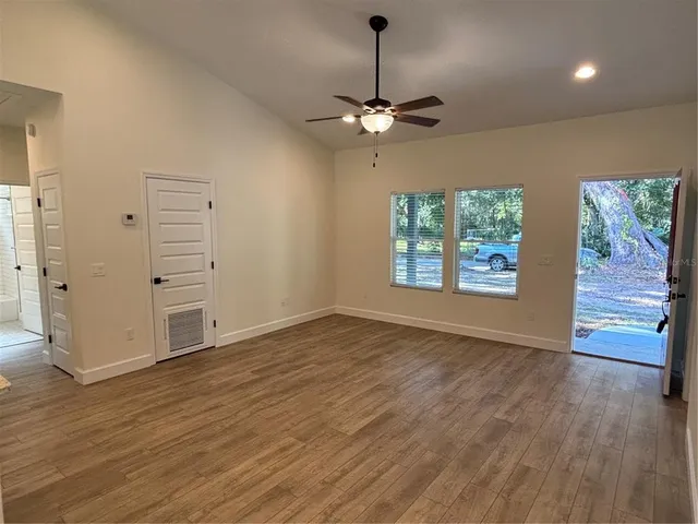 an empty room with wooden floor chandelier and windows