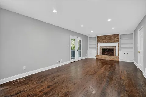 a view of an empty room with wooden floor fireplace and a window
