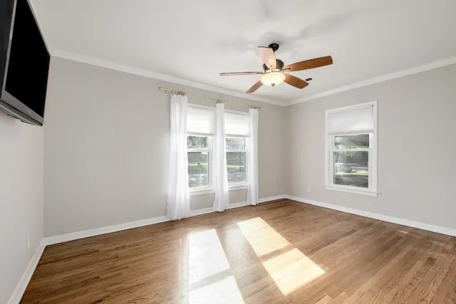 an empty room with wooden floor fan and windows