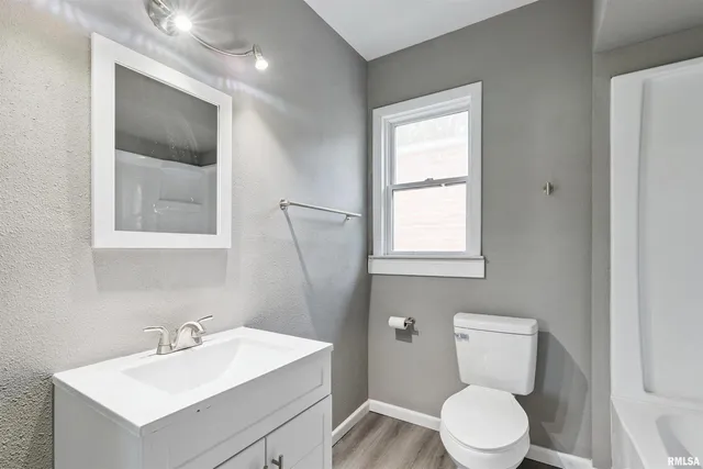 a bathroom with a toilet a sink a mirror and a window