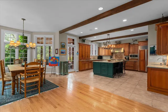 a kitchen with stainless steel appliances kitchen island granite countertop a refrigerator a stove top oven and a dining table with wooden floor