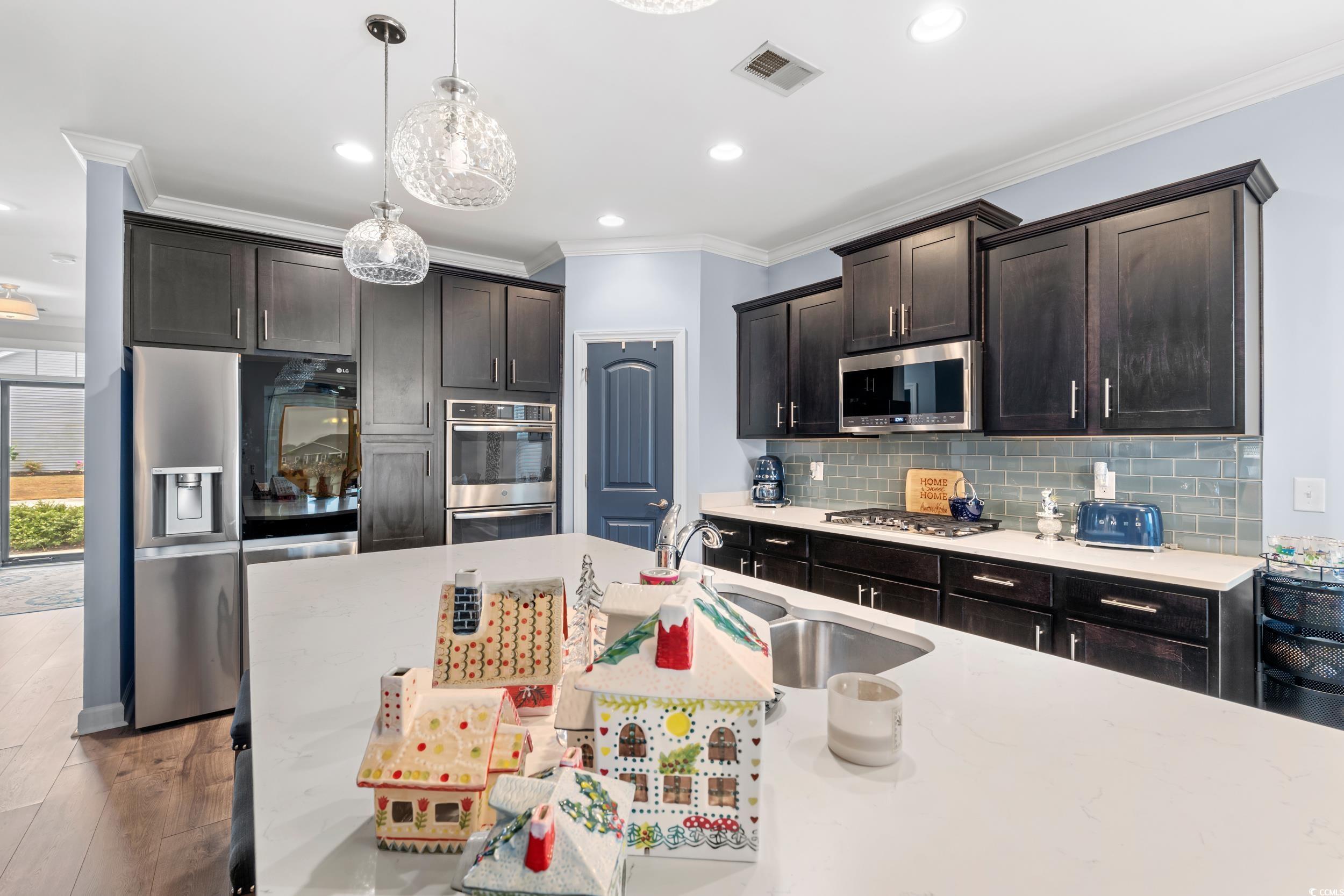 259 Switchgrass Loop Little River, SC 29566 - Photo 7 of 31 Kitchen with dark brown cabinetry, ornamental molding, appliances with stainless steel finishes, hanging light fixtures, and backsplash