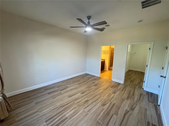 a view of an empty room with wooden floor and a ceiling fan