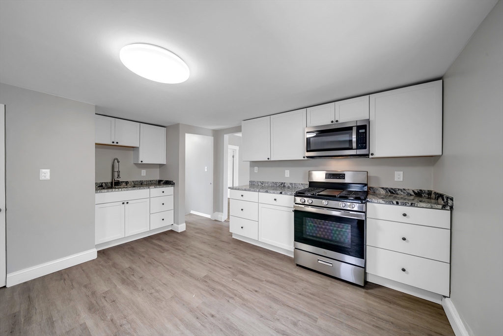 49 6th Street Lowell, MA 01850 - Photo 29 of 37 a kitchen with stainless steel appliances granite countertop a stove top oven a sink dishwasher and a refrigerator with wooden floor