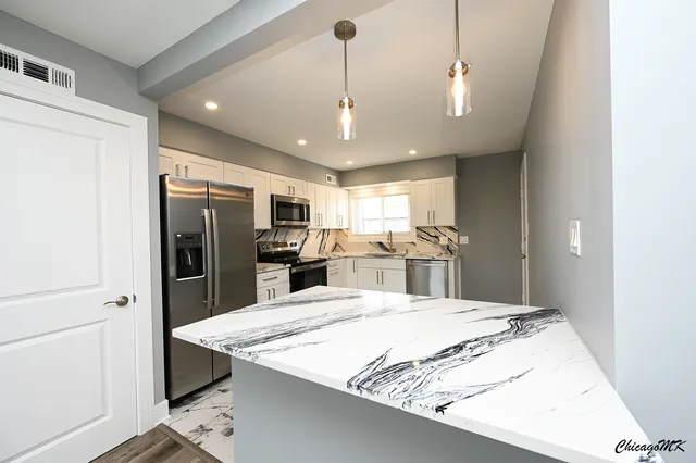 a large kitchen with kitchen island a refrigerator a stove a sink dishwasher a oven with white cabinets and wooden floor